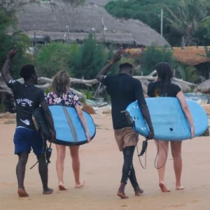 A group of surfers carrying their boards along Praia do Tofo after an exhilarating surf lesson offered by Wutsita Surf School in Tofo, Mozambique.