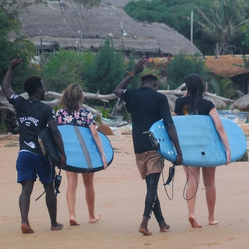 A group of surfers carrying their boards along Praia do Tofo after an exhilarating surf lesson offered by Wutsita Surf School in Tofo, Mozambique.