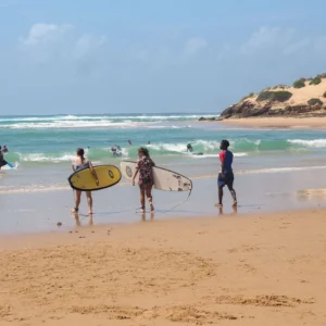 Surfers stand by the shoreline at Praia do Tofo, preparing to catch the waves after renting their surfboards in Wutsita Surf School.